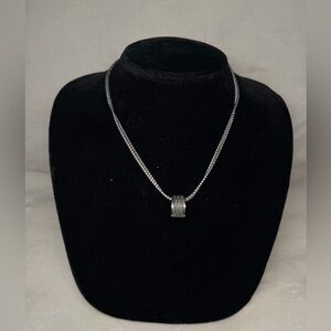 silver necklace with a cylindrical, ringed pendant.